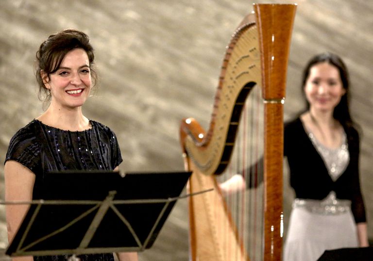 Zwei Musikerinnen nach einer Aufführung von „Lieder in Bildern“. Beide halten Blumen in der Hand. Rechts ist ein Teil einer Harfe zu sehen. Im Hintergrund stehen großformatige Gemälde von Ernst-Martin Heel